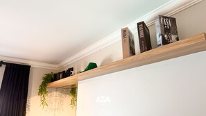 Una estantería de madera con libros y una planta verde frente a una pared con un logotipo.
