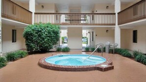 En bygning med flere etager og en central gårdsplads med jacuzzi, omgivet af grønt og flisegulv.