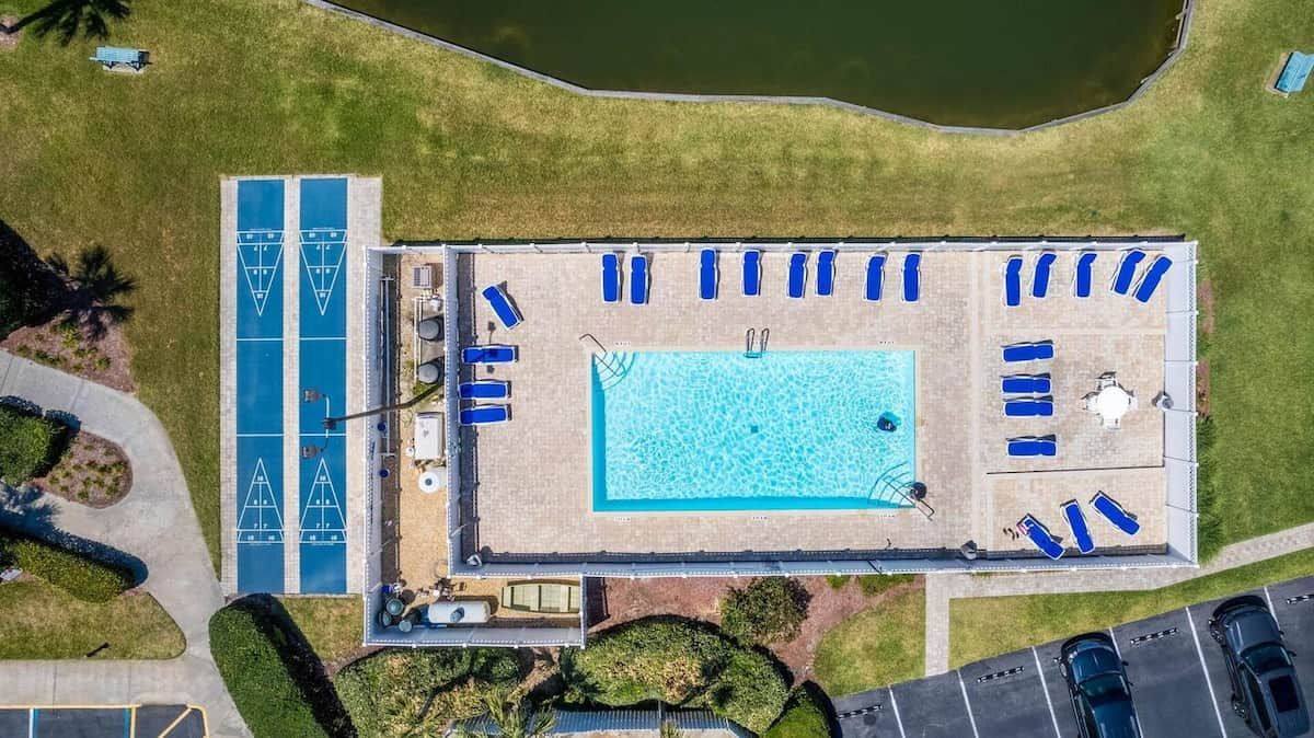 Vue aérienne d’un espace piscine comprenant plusieurs chaises longues et une terrasse distincte autour de la piscine.