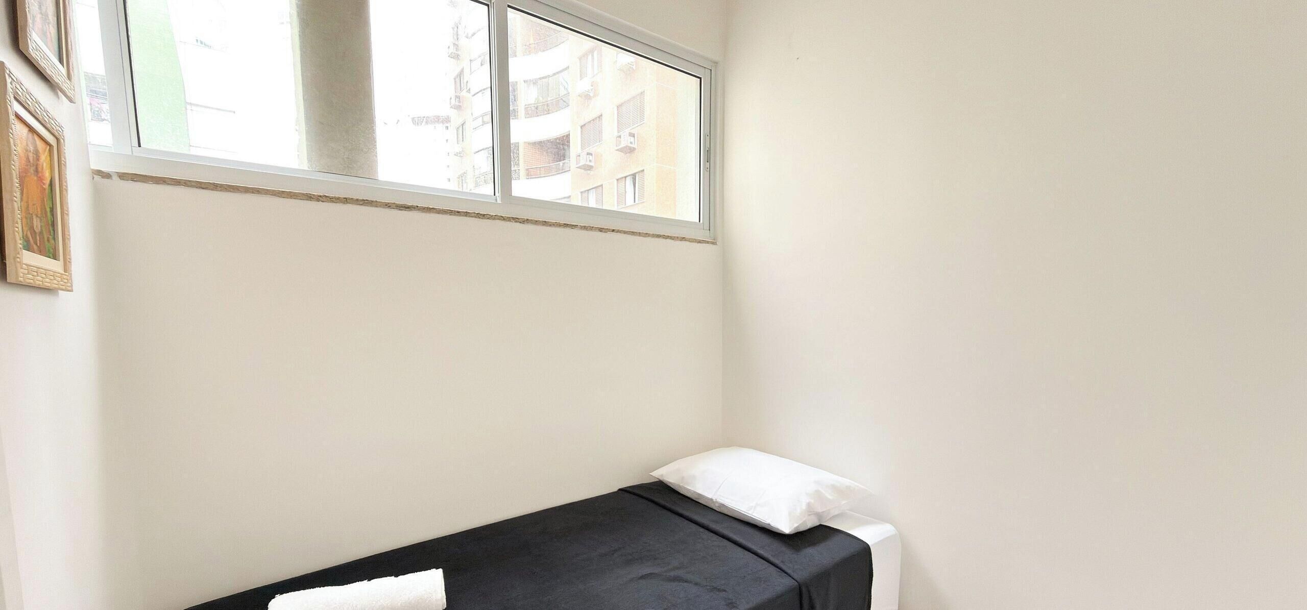 Una habitación pequeña con cama individual, ventana, almohada blanca y un cuadro en la pared.