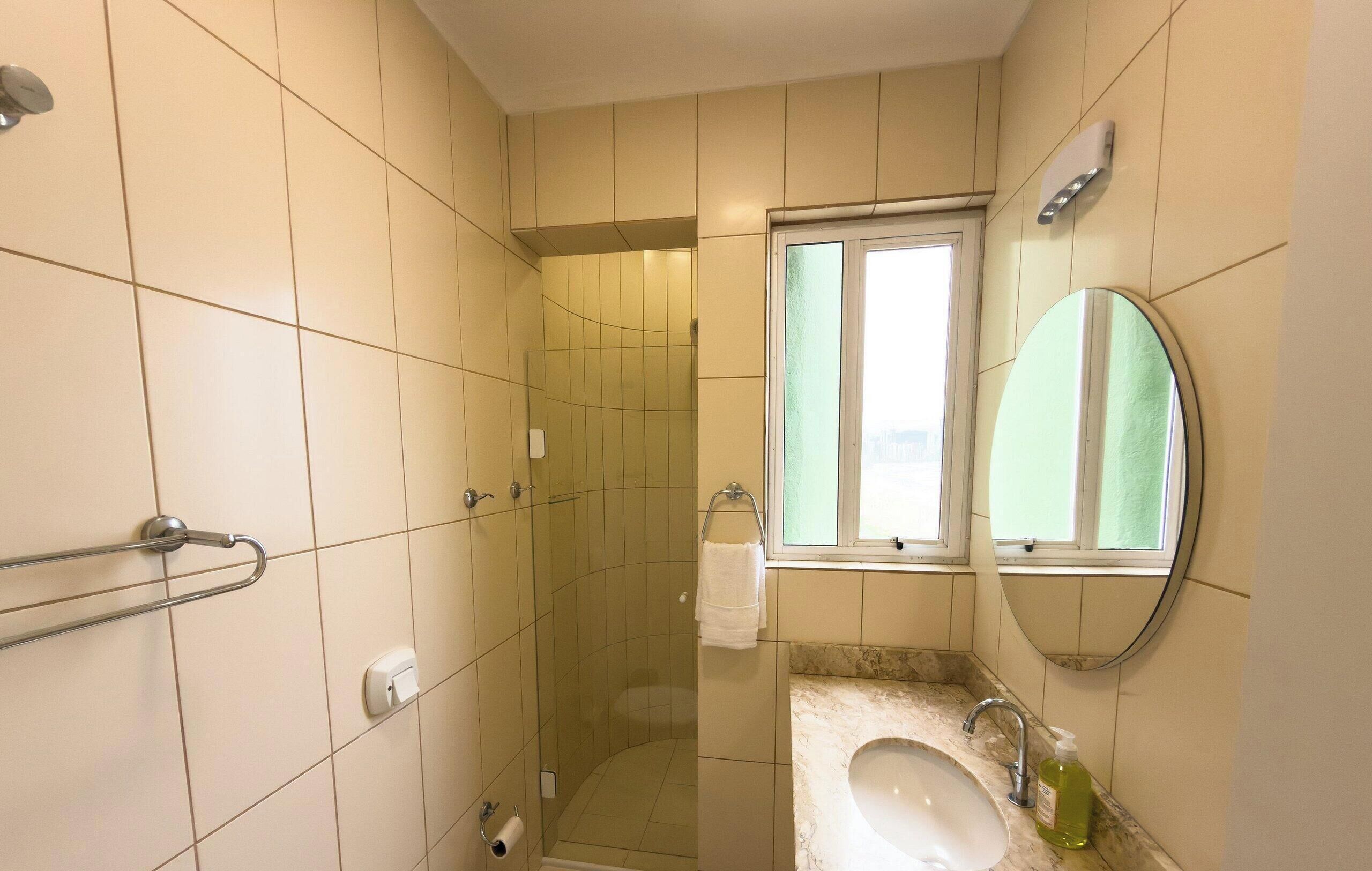 A bathroom with a shower, a sink with a mirror, and a window.
