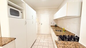A narrow kitchen with white cabinets, a microwave, a stove, and a sink. - ASA Frente Mar Pe na Areia 4QT BC (Balneário Camboriú)