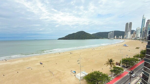 A beach with a clear view of the ocean and a distant mountain. - ASA Frente Mar Pe na Areia 4QT BC (Balneário Camboriú)