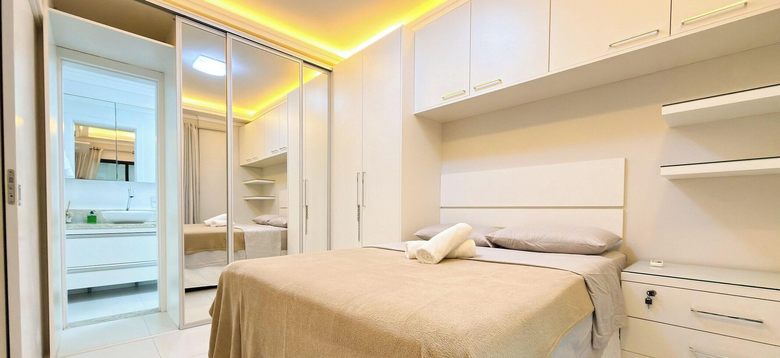 A modern bedroom with a large bed, a walk-in closet, and a bathroom visible through an open door.