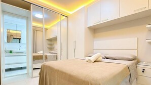 Ein modernes Schlafzimmer mit einem großen Bett, einem begehbaren Kleiderschrank und einem durch eine offene Tür einsehbarer Badezimmer.