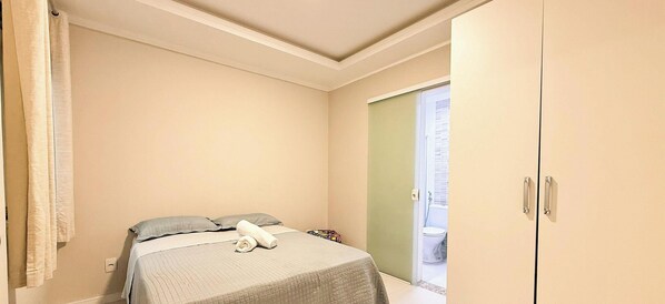 A small, single-bed room with a plain wall, a door leading to a balcony, and a simple bed with a blanket and pillow. - ASA Apto Praia dos Amores 2 Suites BC (Balneário Camboriú)