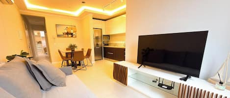 Una sala moderna con televisor de pantalla plana, un sofá, un comedor con sillas y una cocina con refrigerador y microondas.