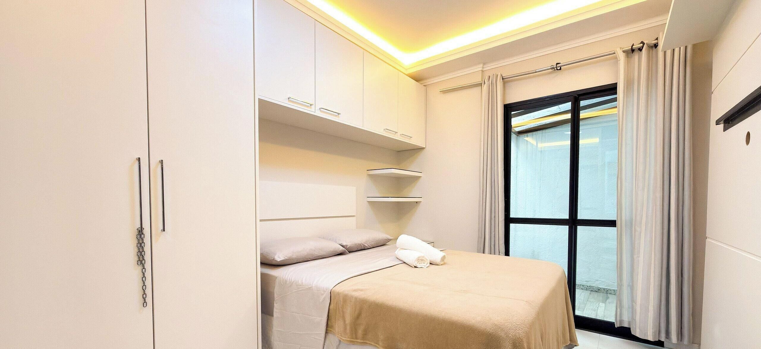 Ein Hotelzimmer mit Bett, Schrank, einem Fenster mit Vorhängen und einer Deckenleuchte.
