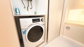 A compact washing machine with a control panel, a water inlet hose, and a detergent dispenser. - ASA Apto Praia dos Amores 2 Suites BC (Balneário Camboriú)