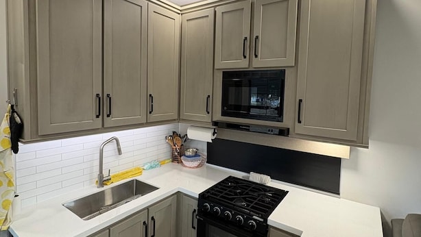 A modern kitchen with grey cabinets, a stainless steel sink, a black stove, and a microwave.