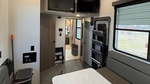 A compact RV interior with a bed, a television, and a window.