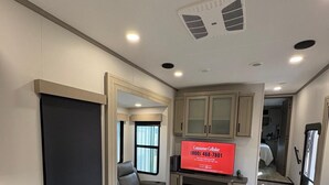 A modern RV interior with a living area, a flat-screen TV, a fireplace, and a kitchen area.