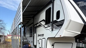 A white recreational vehicle with a covered interior, parked outdoors with a person working on it.