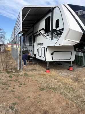 A white recreational vehicle with a covered interior, parked outdoors with a person working on it. - Home away from home in a rural setting with a fully equipped kitchen (Norris City)