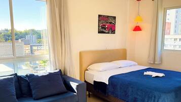 A hotel room with a bed, a sofa, a window with a city view, and a painting on the wall.