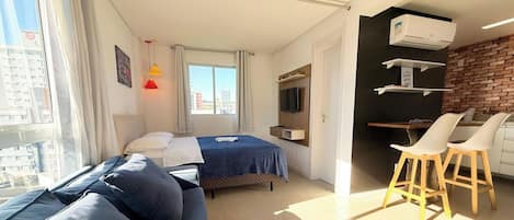 Una habitación de hotel moderna con una cama, un sofá, un escritorio con dos sillas, un televisor y una pared de ladrillo.