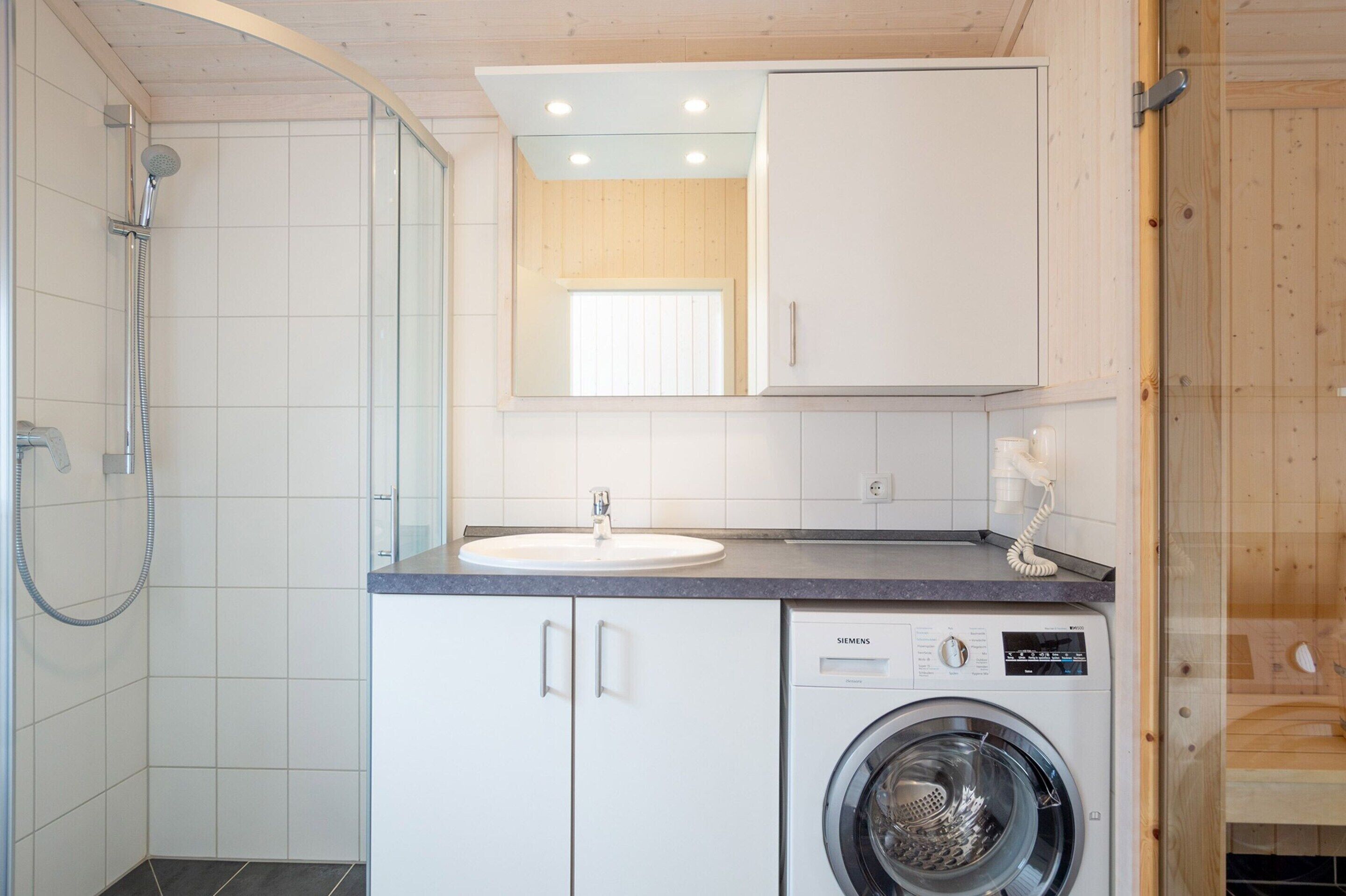 A compact bathroom with a shower, sink, and washing machine.