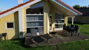 A single-story house with a sloped roof, a patio with a table and chairs, and a small window. - Geraumiges Wellness-zuhause fur 6 Personen (Grossenbrode)