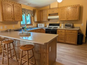 A kitchen with wooden cabinets, a central island with stools, a stove, a microwave, and a toaster. - 3-bedroom family-friendly country home in Galena with air conditioning (Galena)