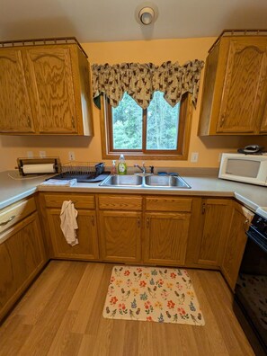 A kitchen with wooden cabinets, a stainless steel sink, a microwave, and a window with a view of trees.