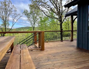 Eine Holzterrasse mit einer Treppe zu einem überdachten Bereich, umgeben von Bäumen und Blick auf die Landschaft.