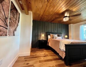 A bedroom with a wooden ceiling, a bed with a dark headboard, two bedside lamps, and a large wooden wall art piece.