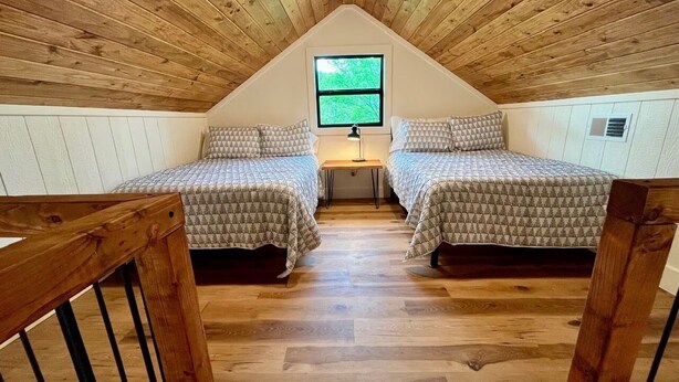 Una habitación con dos camas, una ventana y techo de madera.
