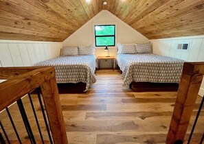 A room with two beds, a window, and a wooden ceiling.