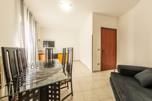 Een moderne woonkamer met een glazen eettafel, zwarte stoelen, een donkere bank en een houten deur.