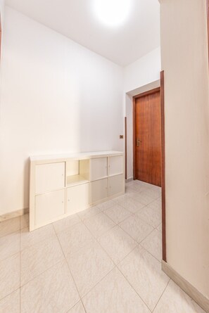 Ein Zimmer mit einer Holztür, einem weißen Schrank mit mehreren Fächern und einem Fliesenboden.