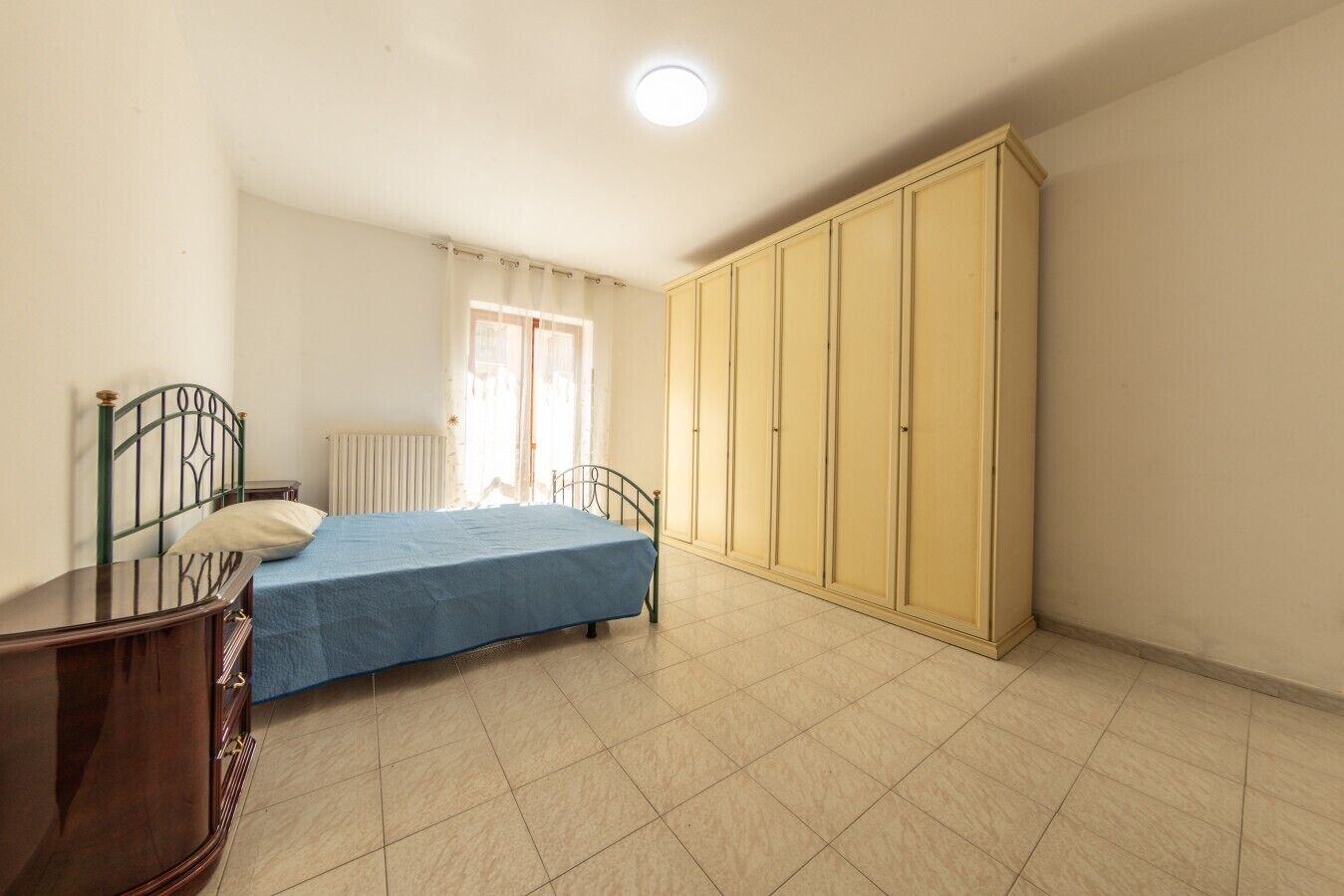 A bedroom with a bed, a wardrobe, a radiator, and a window with curtains.