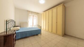 Un dormitorio con cama, armario, radiador y ventana con cortinas.