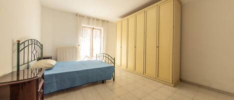 A bedroom with a bed, a wardrobe, a radiator, and a window with curtains.