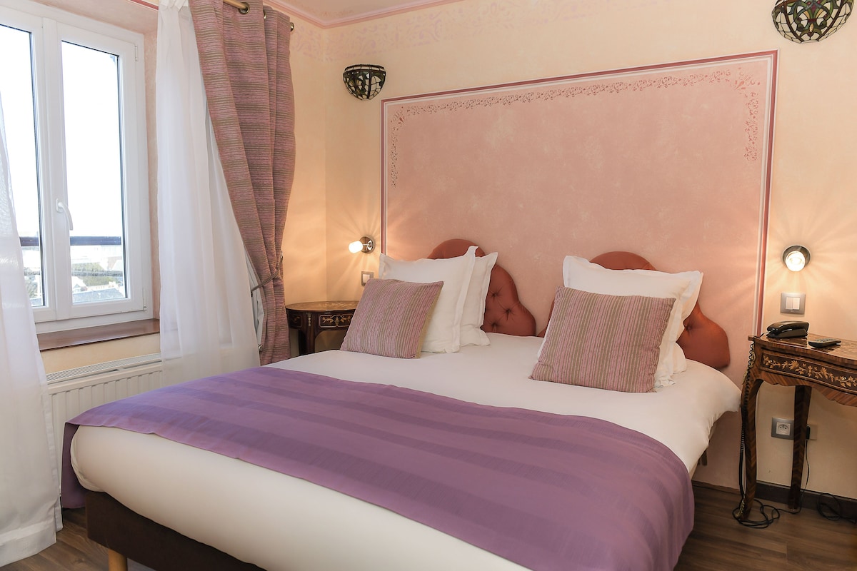 Un dormitorio con una cama grande, dos mesitas de noche, una ventana con cortinas y una lámpara de pared.