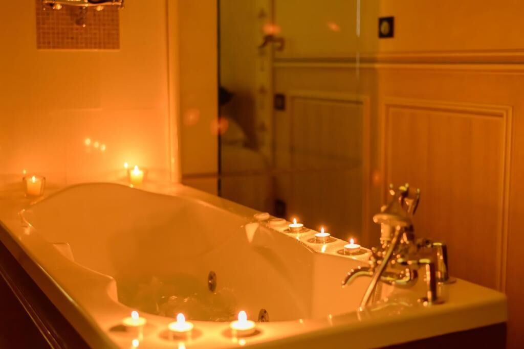 A bathtub with candles, a mirror, and a door in the background.
