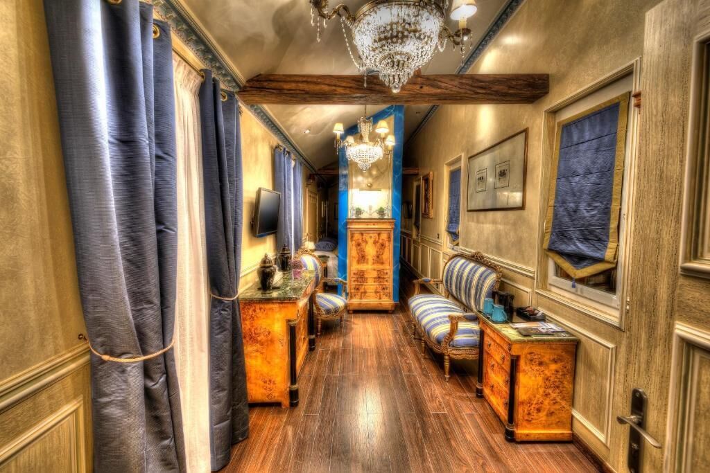 A hallway with a wooden floor, a chandelier, a blue sofa, and a wooden cabinet.