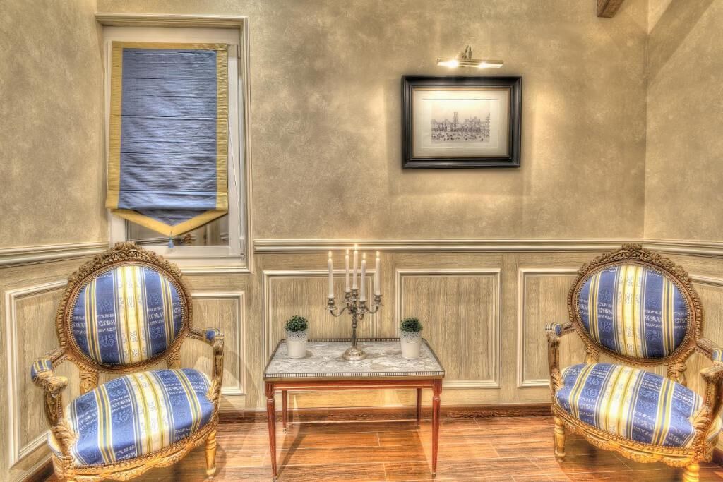 Une pièce comprenant deux fauteuils richement décorés, une table sur laquelle se trouve un chandelier, et un tableau encadré accroché au mur.