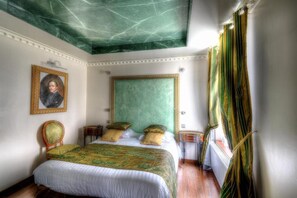 Une chambre à coucher avec un grand lit, une tête de lit verte, un portrait encadré et une fenêtre avec des rideaux.
