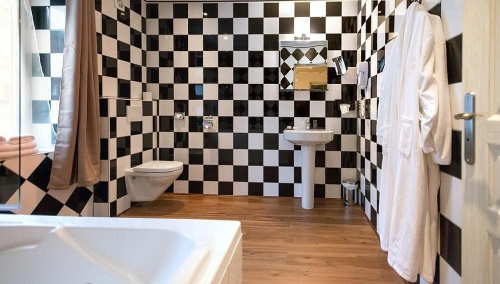 A bathroom with a checkered black and white tile wall, a white sink, a toilet, and a bathtub.