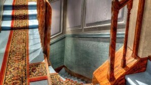 Una gran escalera con barandillas ornamentales y un suelo estampado que conduce a una habitación con un espejo grande y una puerta que indica '4-9'.