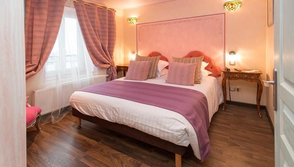 A bedroom with a bed, curtains, a nightstand, and a wall-mounted light fixture.