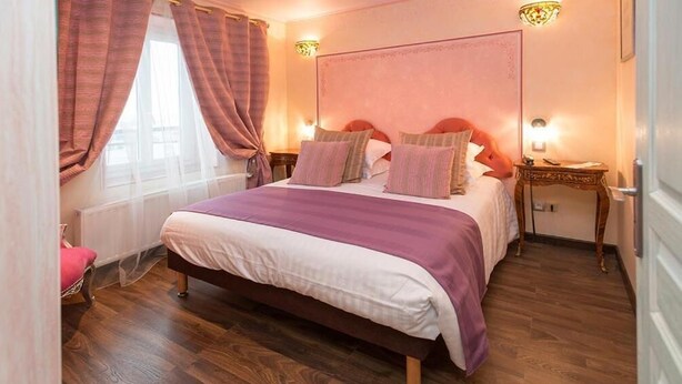 Un dormitorio con cama, cortinas, una mesita de noche y una lámpara de pared.