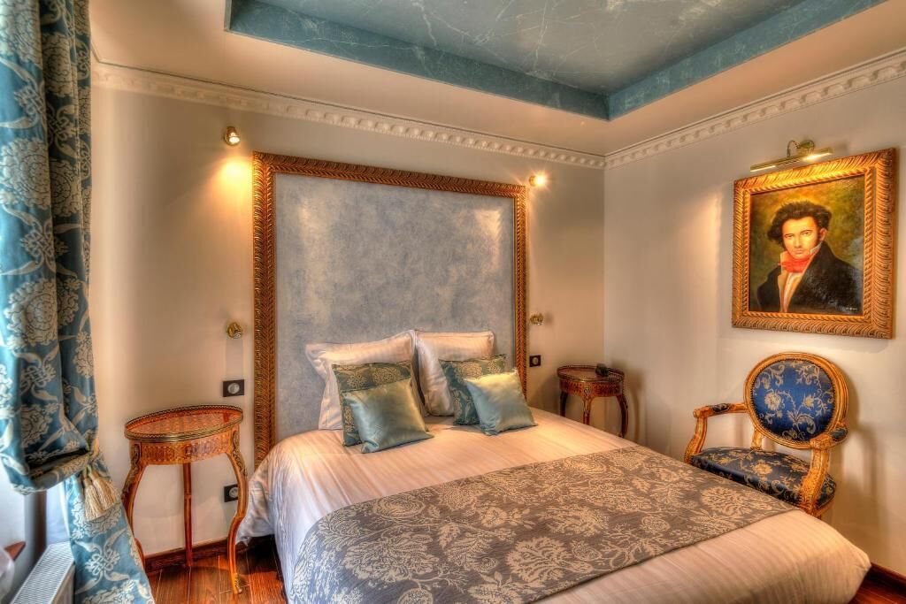 Une chambre avec un grand lit, deux tables de chevet, une chaise, un tableau au mur et une couvre-lit à motifs.