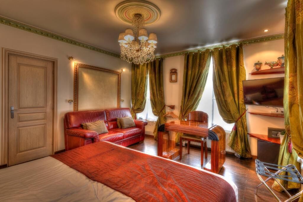 Una habitación de hotel con una cama grande, un sofá de cuero rojo, una mesa de madera y un televisor.