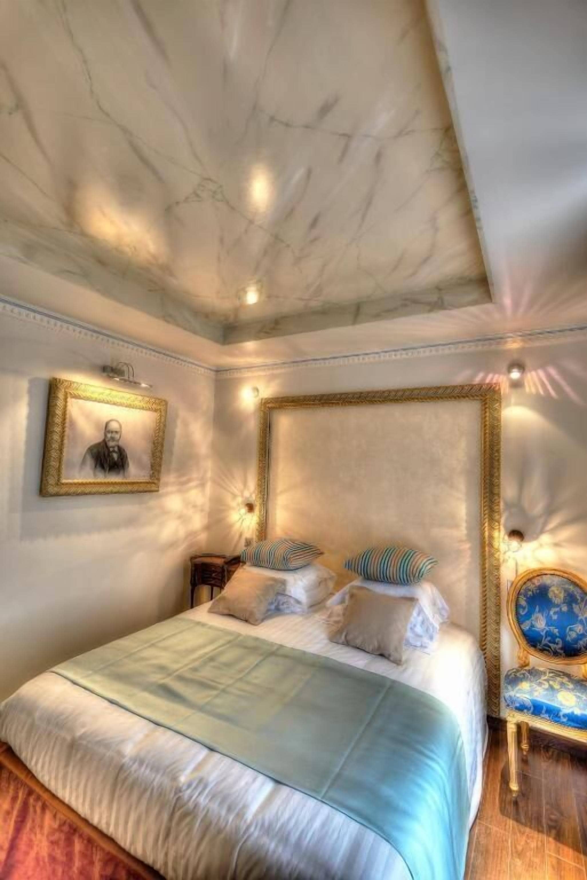 Une chambre à coucher avec un grand lit, une tête de lit, une table de chevet, une chaise et un tableau encadré au mur.