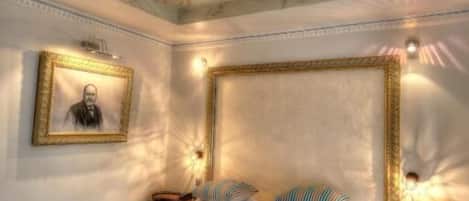 A bedroom with a large bed, a headboard, a nightstand, a chair, and a framed picture on the wall.