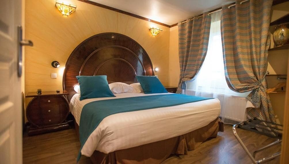 Una camera d'albergo con un letto grande, una testiera in legno e vista sul mare attraverso le tende.