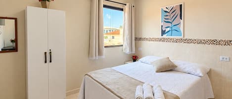 Habitación de hotel con cama, armario, equipo de aire acondicionado, ventana con cortinas y una obra de arte colgada en la pared.