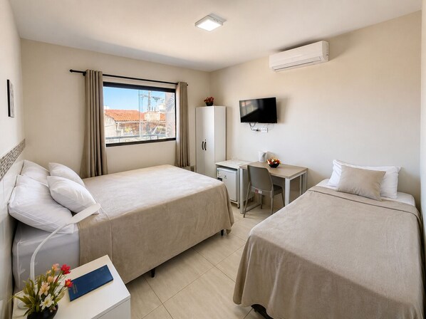 A hotel room with two beds, a desk, a TV, and a window with curtains.