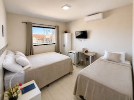 Quarto de hotel com duas camas, uma escrivaninha, uma televisão e uma janela com cortinas.